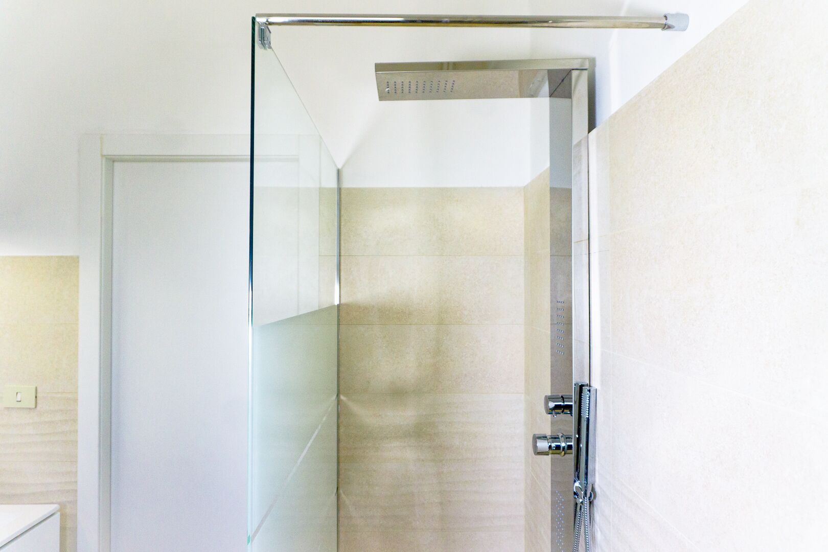 A glass-enclosed shower with a chrome handle and a control panel.