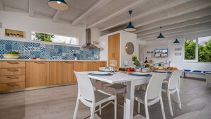 A modern kitchen with a dining area, featuring a large island, white cabinetry, and blue patterned backsplash.