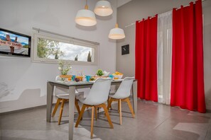 Ein Essbereich mit einem Tisch für vier Personen, einem an der Wand montierten Fernseher und einem Fenster mit Blick auf Bäume.