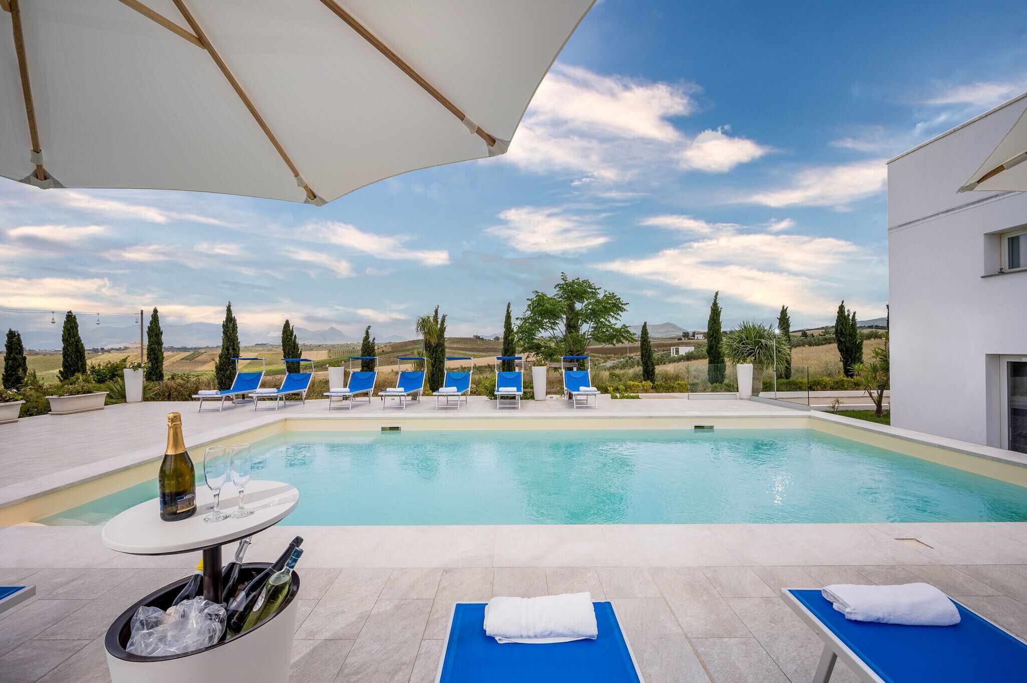 Un espace piscine avec des chaises longues, une table avec une bouteille et des verres, et une vue sur la campagne.