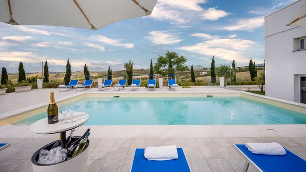 A pool area with lounge chairs, a table with a bottle and glasses, and a view of the countryside.