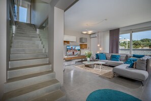 A modern living room with a staircase, a sofa set, and a television.