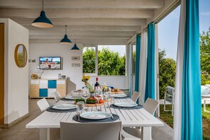 A dining area with a table set for six, a television, and a view of greenery outside.