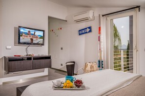 Ein Hotelzimmer mit Bett, Fernseher der ein Reisebild zeigt, einem 'ONE WAY'-Schild und Blick auf Grün durch das Fenster.