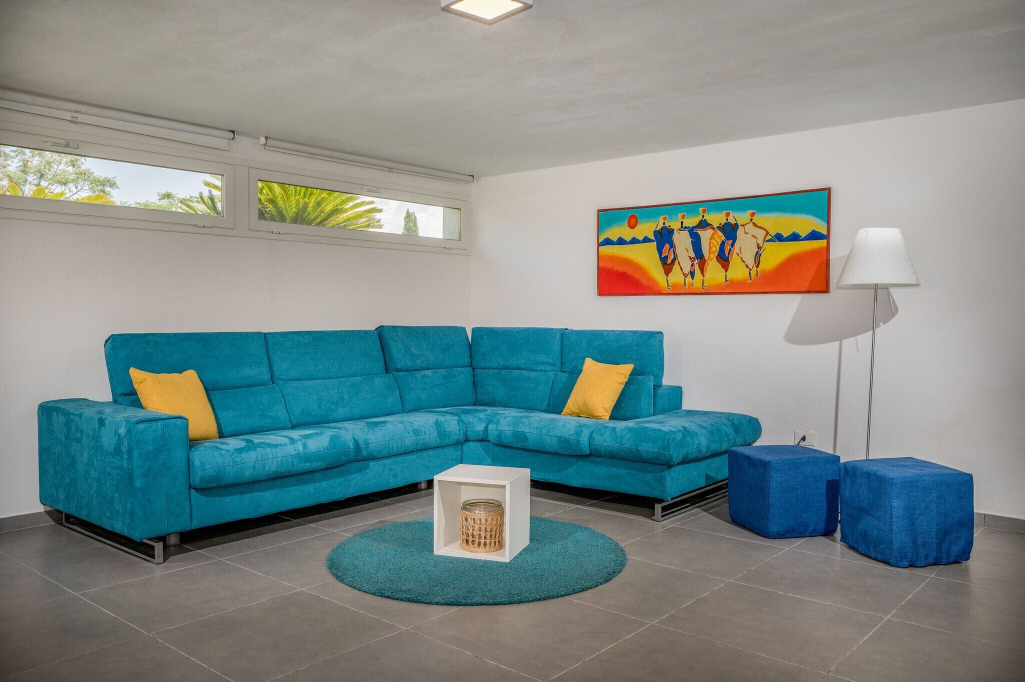 A modern living room with a teal sectional sofa, a small white side table, a teal rug, and a floor lamp.