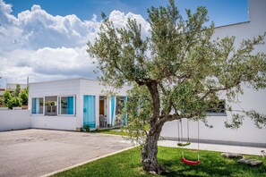 A modern building with a white exterior, a tree in the foreground, and a swing set.