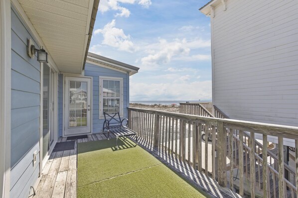 A wooden deck with a green mat, a white railing, and a view of the beach.