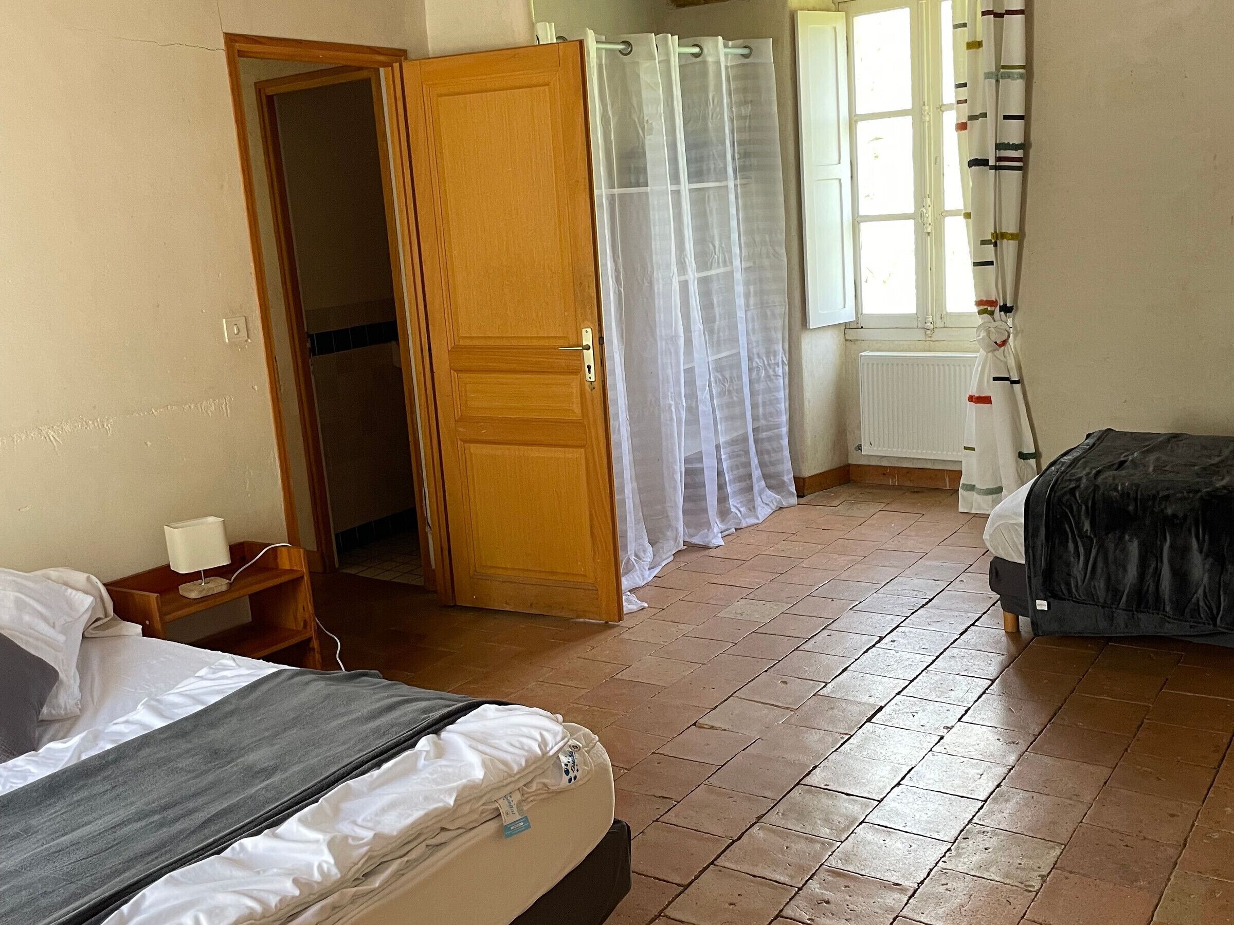 Ein Schlafzimmer mit einem Bett, einem Nachttisch, einer Holztür, einem Fenster mit Vorhängen und einer Heizung.