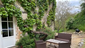 A patio with wicker furniture, a white door, and a stone wall covered in ivy.