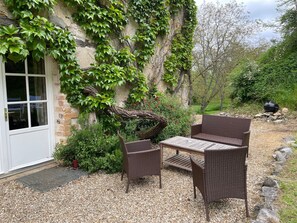 A patio with wicker furniture, a white door, and a stone wall covered in ivy.
