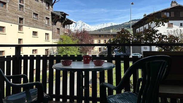 A balcony with a table and chairs, overlooking a mountain and buildings. - Charming T3 in Combloux Center - Pets and Parking Included (Combloux)