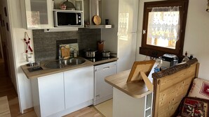 A compact kitchen with a microwave, stove, sink, and a small wooden table. - Charming T3 in Combloux Center - Pets and Parking Included (Combloux)