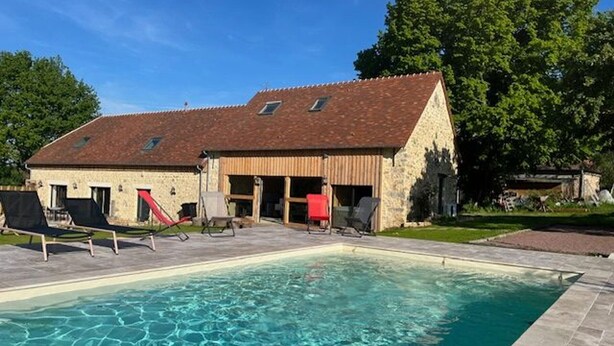 Zona de piscina con un edificio de piedra, sillas exteriores y un tobogán.