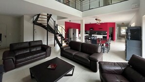 Amplia sala de estar con techo alto, una escalera y un comedor con detalles en rojo.
