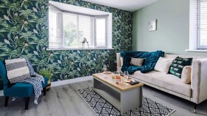 A living room with a patterned wallpaper, a sofa, a coffee table, and a window with blinds. - One-bedroom by Media City UK by Belvilla (Manchester)