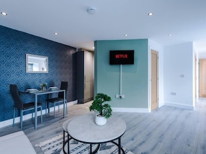 A modern living room with a dining area, a mounted TV, and a potted plant. - One-bedroom by Media City UK by Belvilla (Manchester)