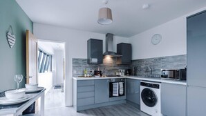 A modern kitchen with grey cabinets, a built-in washing machine, and a dining area with a table and chairs. - One-bedroom by Media City UK by Belvilla (Manchester)