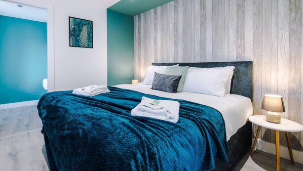 A modern hotel room with a large bed, teal walls, and a wooden accent wall. - One-bedroom by Media City UK by Belvilla (Manchester)