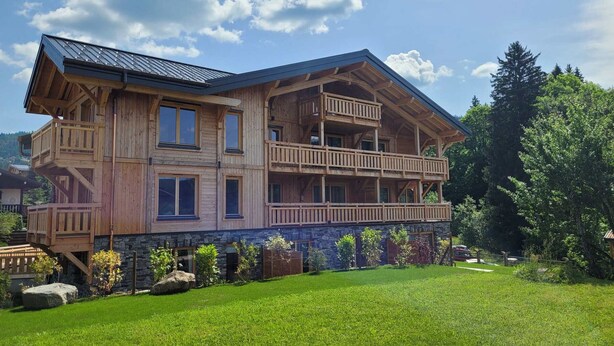 Ein mehrstöckiges Holzchalet mit Balkonen, Stein Fundament und einem gepflegten Rasen.