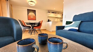 Ein modernes Wohnzimmer mit einem blauen Sofa, einem Esstisch mit Stühlen und drei blauen Keramiktassen auf einem strukturierten Tisch.