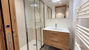 Ein modernes Badezimmer mit Duschkabine aus Glas, einem Holzkosmetikschrank mit Waschbecken und einem Spiegel darüber.