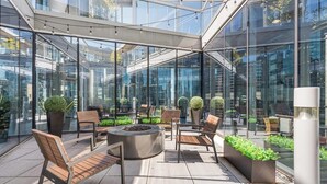 A modern outdoor lounge area with glass walls, wooden furniture, and potted plants. - High-End 3BR Retreat + Steps to Millennium Park (Chicago)