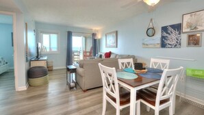 Ein Wohnzimmer mit Esstisch, weißen Stühlen, Deckenventilator und Sofa.