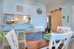 Un comedor con una mesa de madera, sillas blancas y caminos de mesa azules.