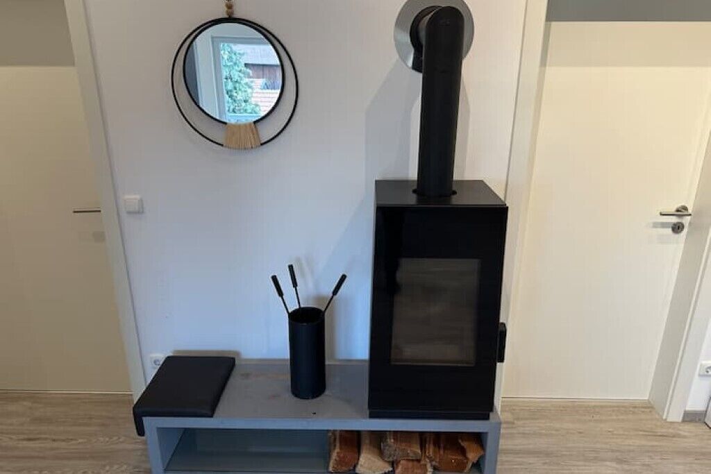 A modern room with a built-in wood stove, a small shelf with a black container, and a round mirror on the wall.