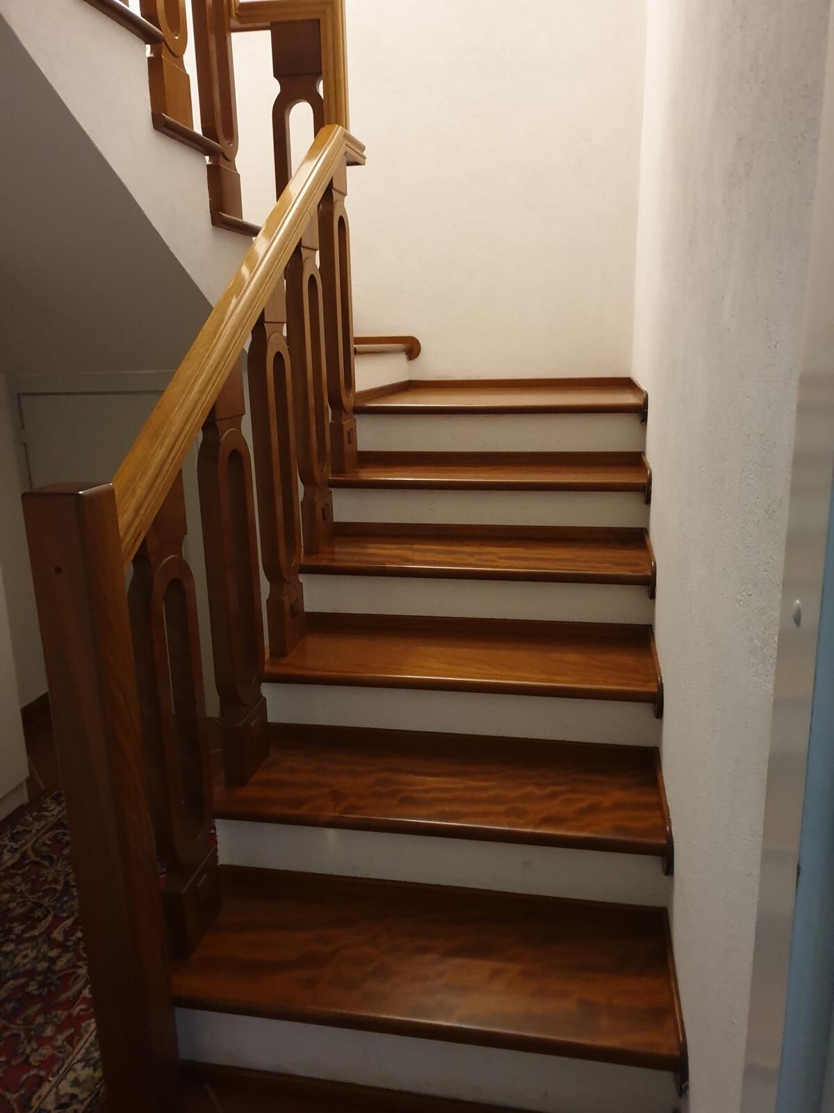 Una escalera de madera con paredes blancas y piso alfombrado.
