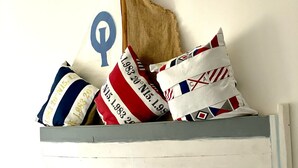 Un lit avec une literie blanche, une tête de lit sur le thème de la marine et des coussins décoratifs aux motifs et couleurs variés.