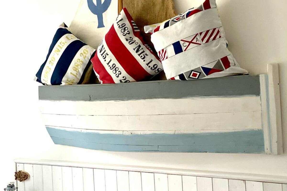 Un lit avec une literie blanche, une tête de lit sur le thème de la marine et des coussins décoratifs aux motifs et couleurs variés.