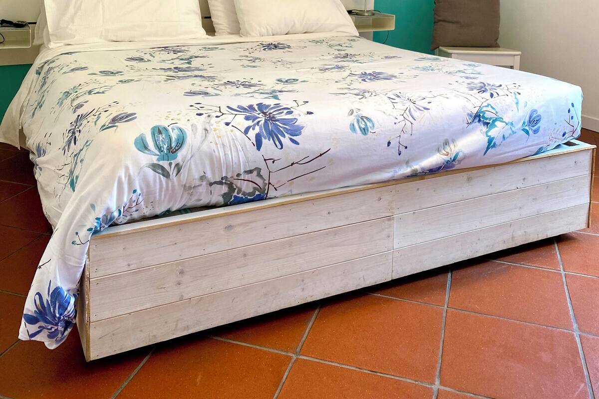 Une chambre à coucher avec un lit, une tête de lit blanche et une fresque représentant un paysage de montagne sur le mur.