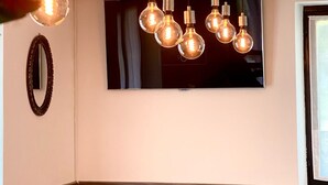 Un coin repas agrémenté d’un lustre moderne, d’un téléviseur à écran plat fixé au mur et d’un mur d’accent en bois.