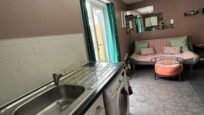 Une cuisine compacte comprenant un évier, un lave-linge et un coin repas avec un canapé et une petite table.