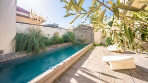 Ein Swimmingpool mit einer gefliesten Kante, umgeben von Olivenbäumen und einem kleinen Garten.