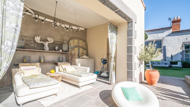 Un patio soleado con un sofá blanco, una mesita pequeña y una cabeza de venado decorativa.