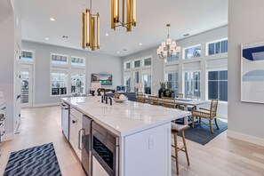 A spacious kitchen with a large island, modern appliances, and a dining area with wooden chairs and a chandelier. - Grand Poolside Home@Cinnamon Shore South Near Beach, Lake & More Amenities (Port Aransas)