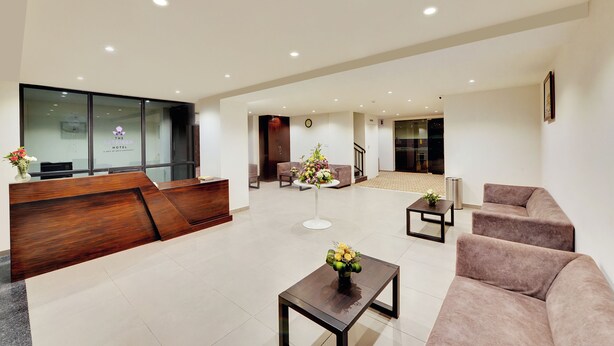A hotel reception area with a wooden reception desk, a seating area with sofas, and a small table with a vase of flowers. - The Lavender Hotel (Bengaluru)