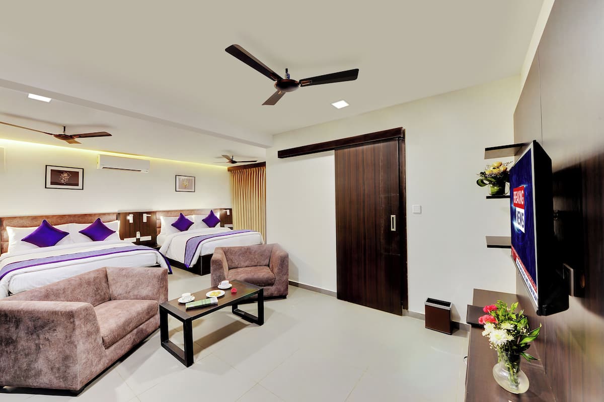 A hotel room with two beds, a sofa, a coffee table, a TV, and a wardrobe.