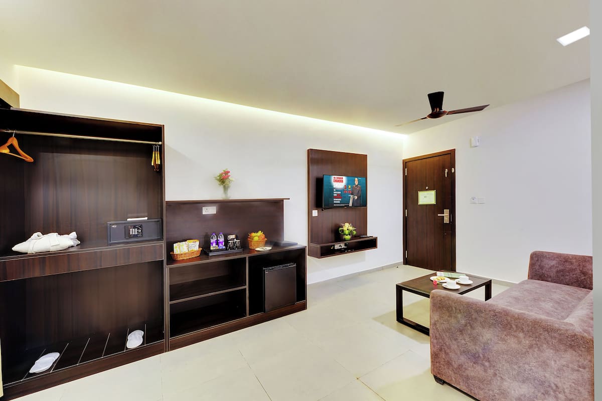 A modern hotel room with a large wardrobe, a flat-screen TV, a small table, and a comfortable sofa.