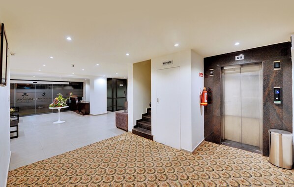 A hotel lobby with a patterned carpet, a private elevator, and a reception area with a small table and chairs.