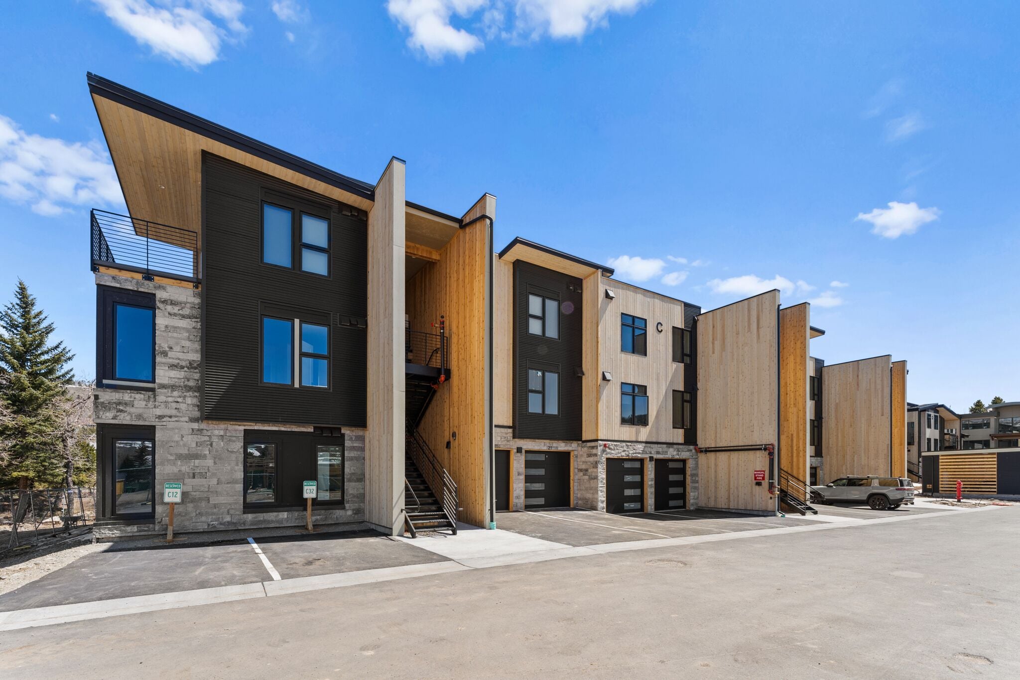 A modern multi-story building with a mix of wood and stone facades, multiple garage doors, and a clear sky.
