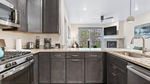 A modern kitchen with dark cabinets, a stainless steel stove, and a large window overlooking a garden.