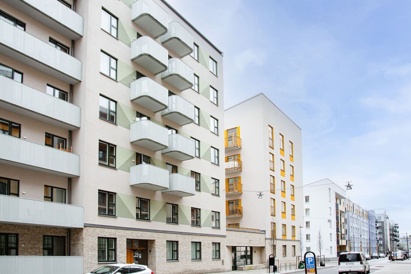 A multi-story residential building with balconies, a ground-level entrance, and a parking sign.