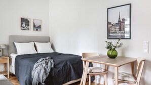 Ein Schlafzimmer mit Bett, Nachttisch, Lampe und einem Stadtbild im Bilderrahmen an der Wand.
