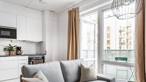 Ein modernes Apartment mit grauem Sofa, einer Küche mit weißen Schr änken und Blick auf Gebäude durch große Fenster.