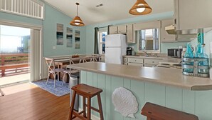 Uma cozinha moderna com uma ilha grande, luminárias pendentes e vista para o oceano.