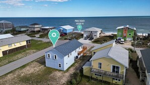 Zona residencial costeira com casas, acesso público à praia e o oceano ao fundo.