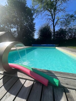 Relax by the pool surrounded by lush greenery and a deck.
